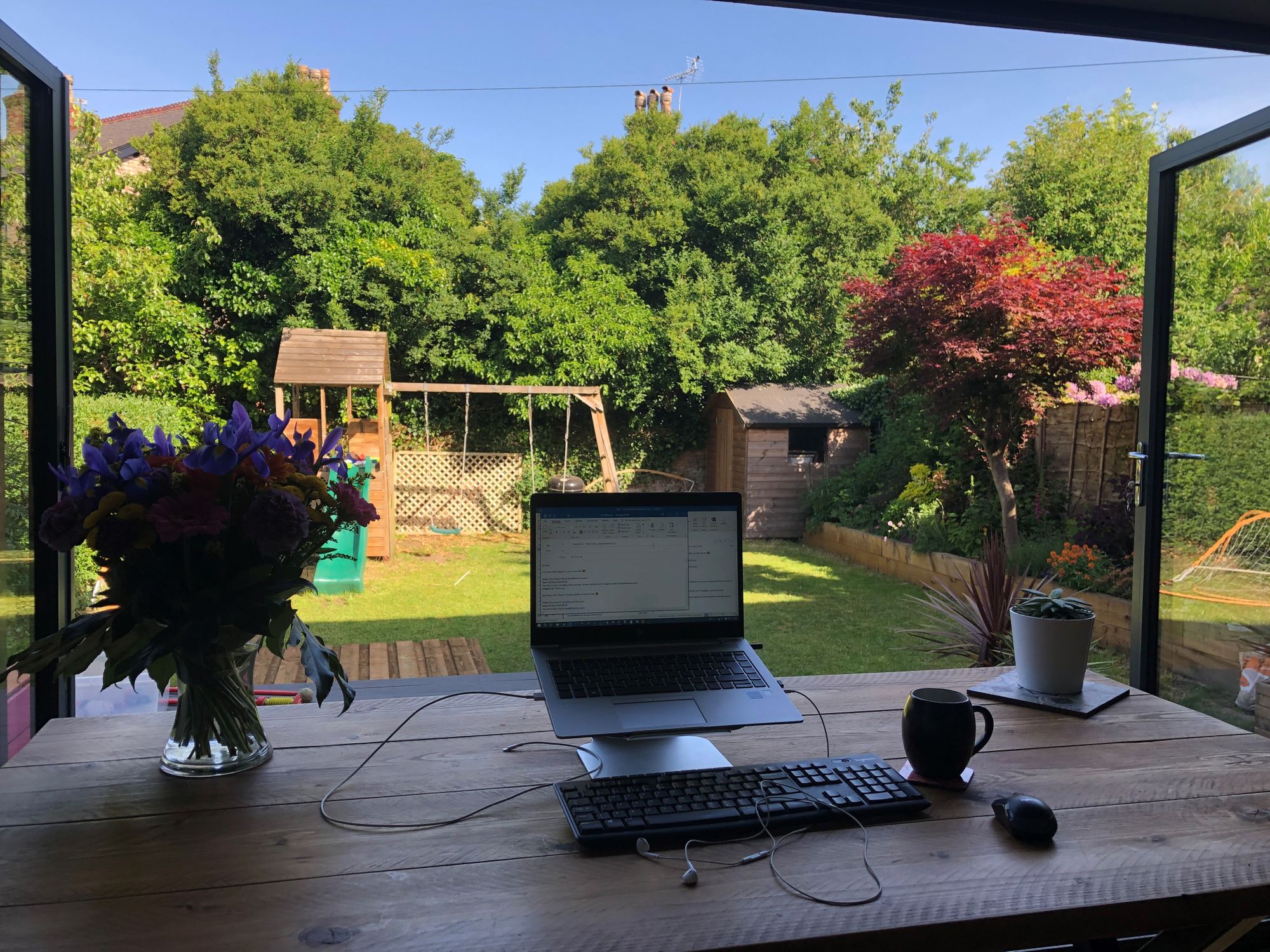 Laptop on table facing back garden with children's swing and slide